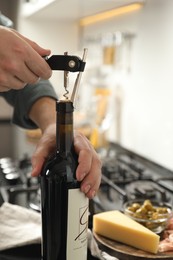 Photo of Man opening wine bottle with corkscrew indoors, closeup