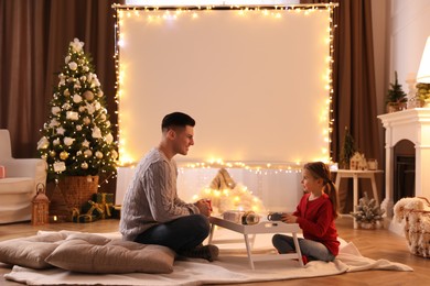 Photo of Father and daughter near video projector screen at home. Cozy Christmas atmosphere