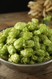 Photo of Fresh green hops in sieve on wooden table, closeup