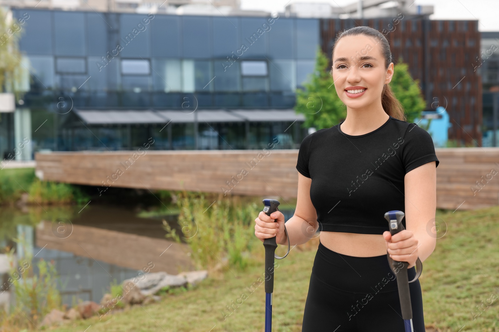 Photo of Young woman practicing Nordic walking with poles outdoors. Space for text