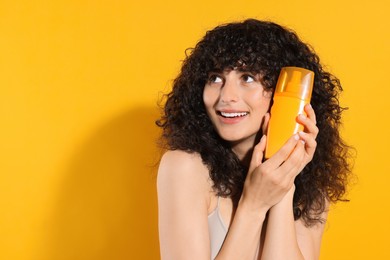 Photo of Beautiful young woman holding bottle of sun protection cream on orange background, space for text