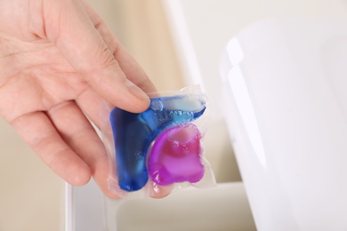 Photo of Woman putting laundry detergent capsule into washing machine, closeup