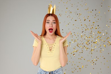 Photo of Emotional young woman with princess crown under falling confetti on light grey background