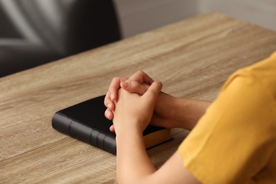 Photo of Religious woman praying over Bible at wooden table indoors, closeup