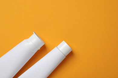 Photo of Blank tubes of toothpaste on orange background, flat lay. Space for text