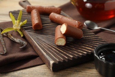 Photo of Glazed curd cheese bars, vanilla pods and flower on wooden table, closeup