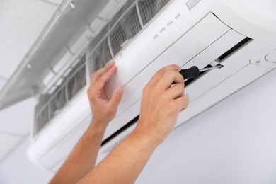 Photo of Professional technician maintaining modern air conditioner indoors, closeup