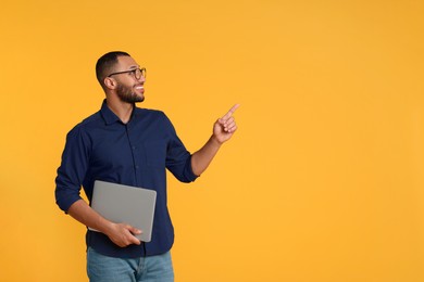 Photo of Smiling young man with laptop on yellow background, space for text