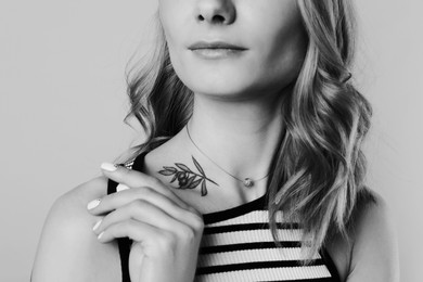 Image of Young woman with tattoo on light background, closeup. Black and white photography