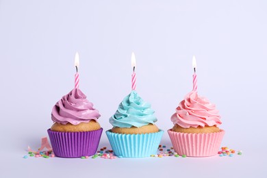 Photo of Delicious birthday cupcakes with burning candles and sprinkles on light grey background