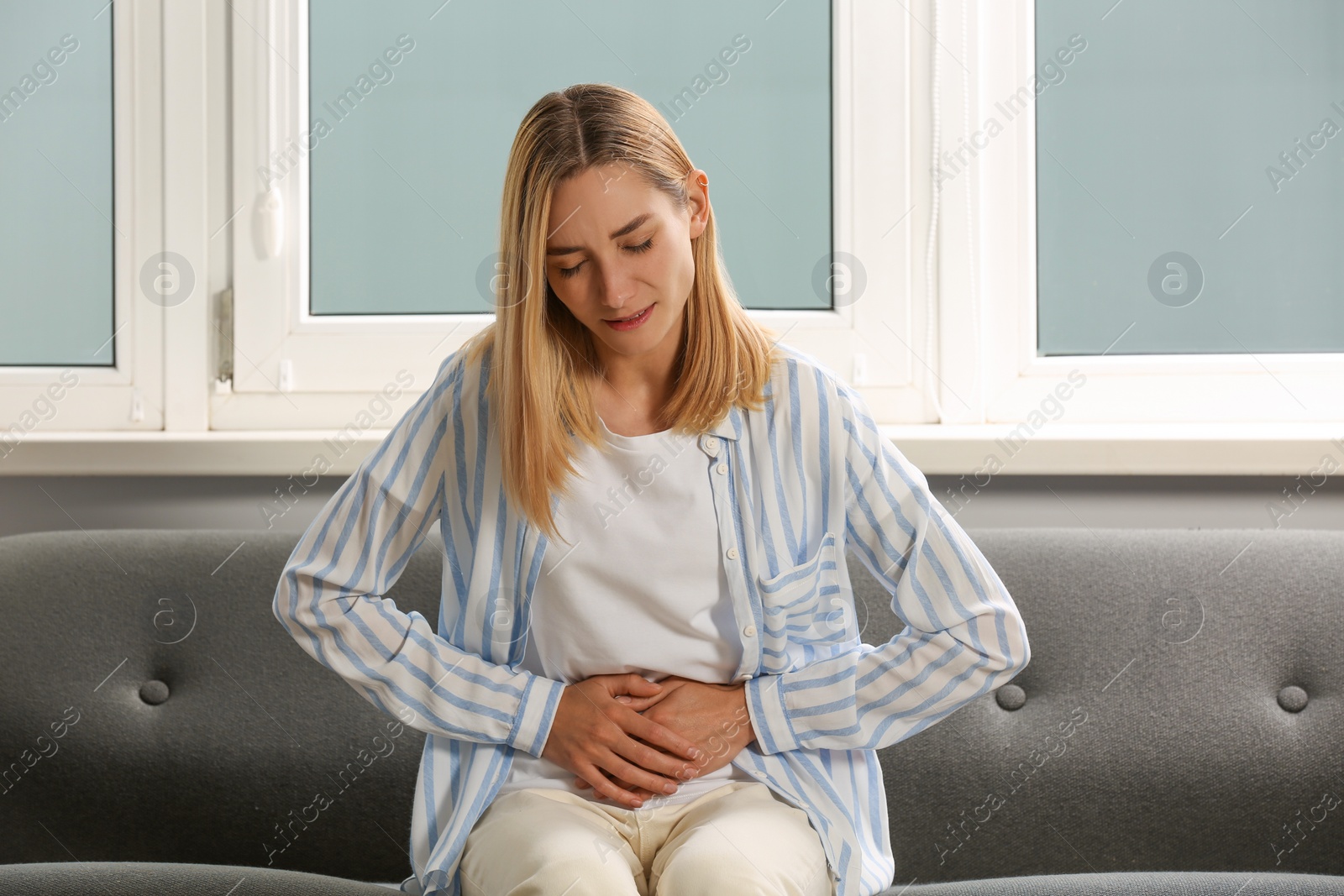 Photo of Young woman suffering from menstrual pain on sofa indoors