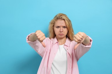Photo of Dissatisfied young woman showing thumbs down on light blue background