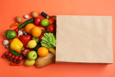 Photo of Paper bag with different groceries on coral background, flat lay