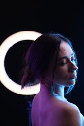 Photo of Beautiful woman and ring lamp on dark background in neon lights