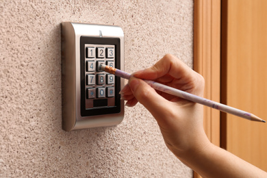 Photo of Woman using pencil to enter code on electronic lock's keypad indoors, closeup