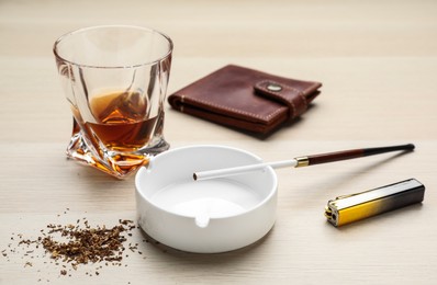 Ashtray with long cigarettes holder, lighter, wallet and alcohol drink on wooden table