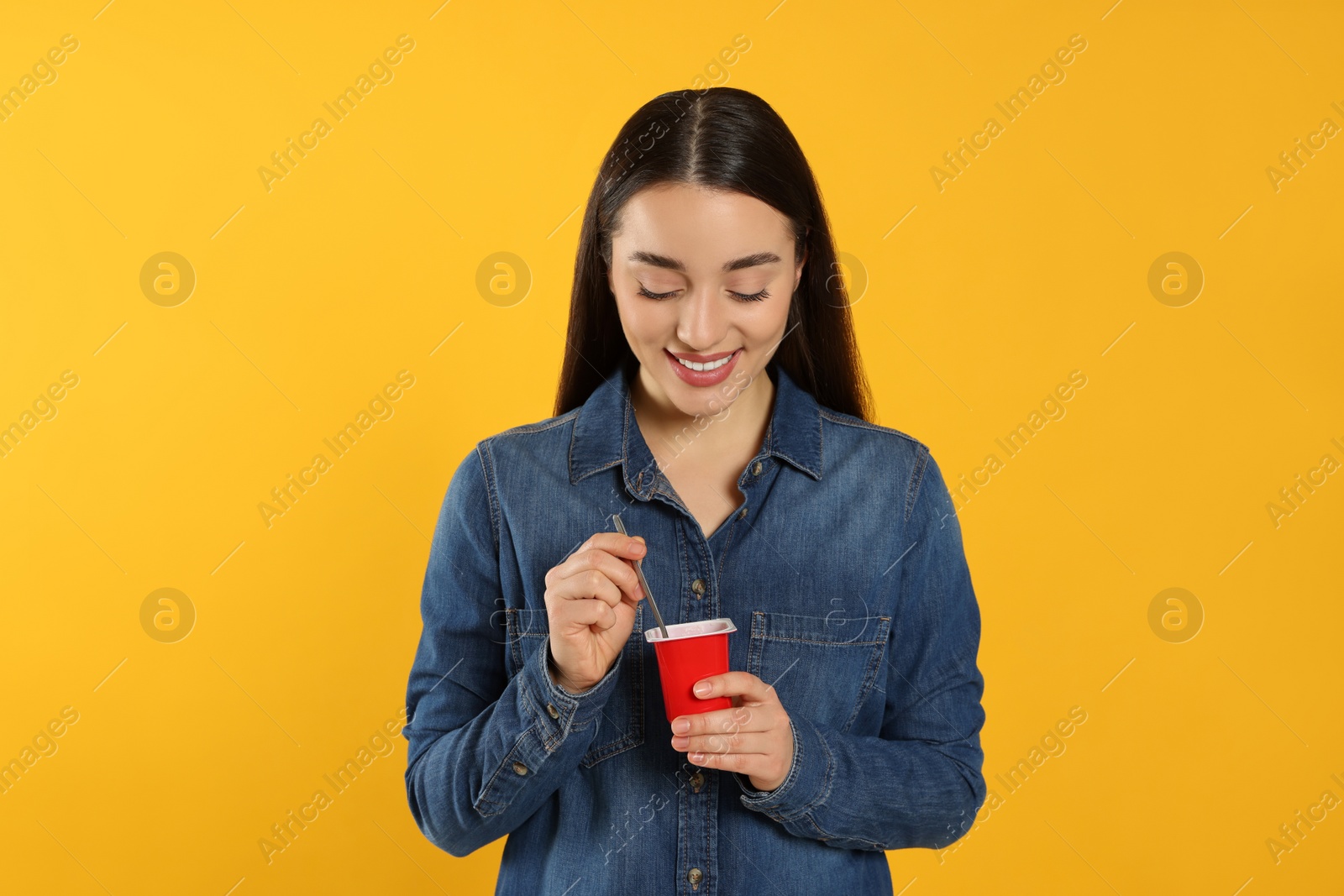 Photo of Happy woman with tasty yogurt on orange background