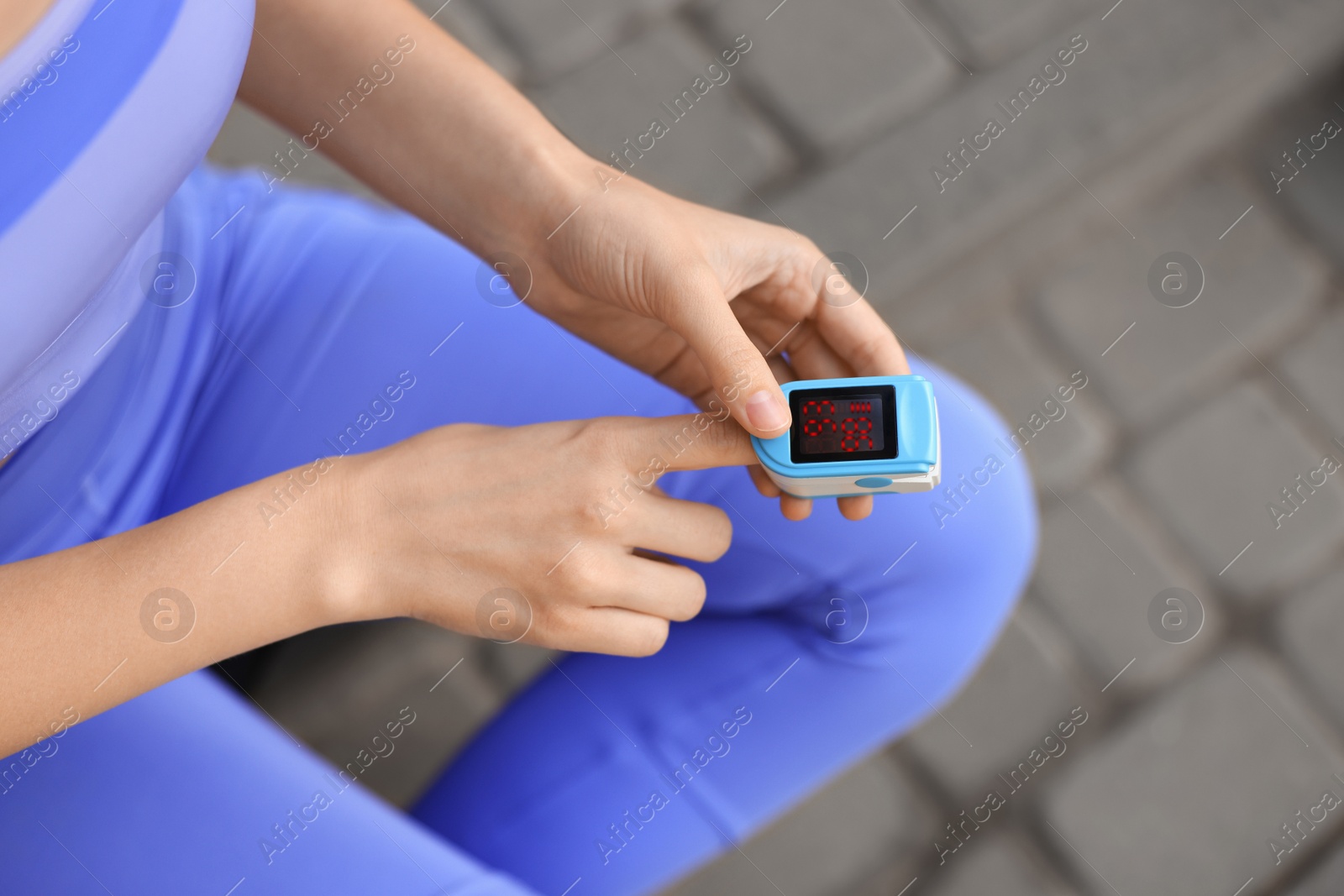 Photo of Woman checking pulse with blood pressure monitor on finger after training outdoors, closeup