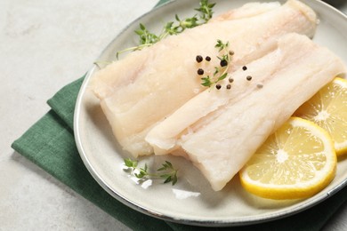 Photo of Plate with raw cod fish, spices, microgreens and lemon on grey table, closeup