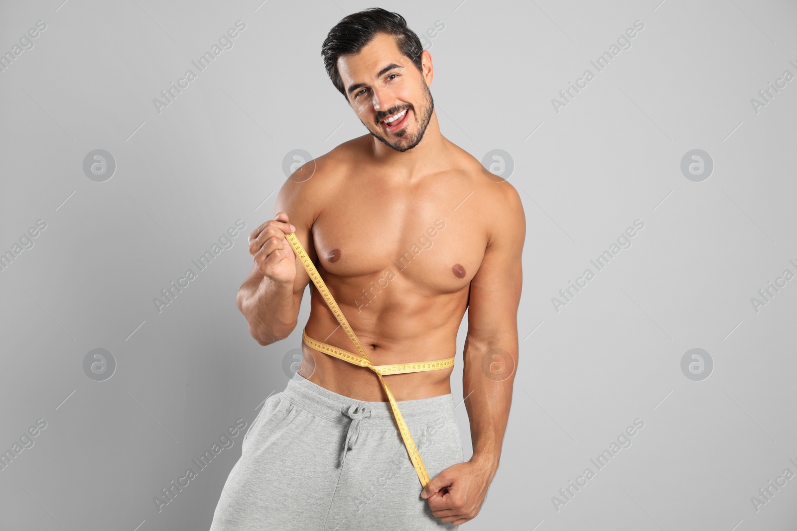 Photo of Young man with slim body using measuring tape on grey background