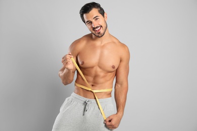 Young man with slim body using measuring tape on grey background