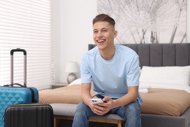 Smiling guest with smartphone and suitcase in stylish hotel room