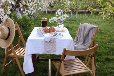 Photo of Stylish table setting with beautiful spring flowers, tea and croissants in garden