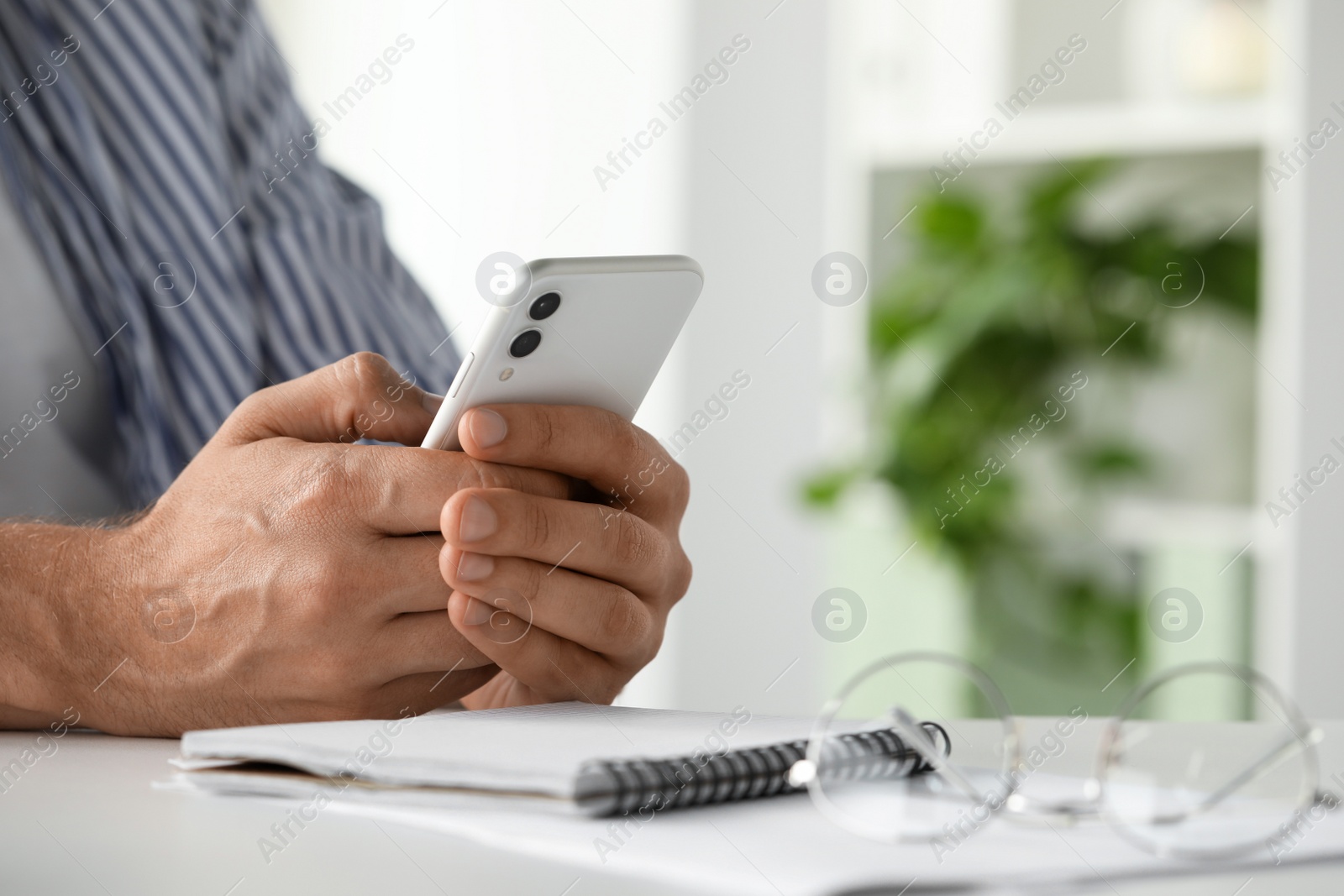 Photo of Man sitting at table and using smartphone in room, closeup. Space for text