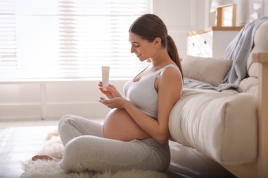 Photo of Young pregnant woman with cosmetic product at home