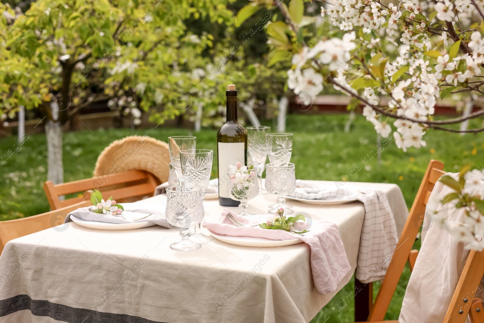 Photo of Stylish table setting with beautiful spring flowers, wine, plates and glasses in garden