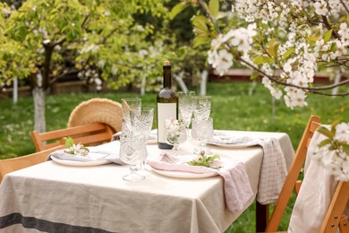 Stylish table setting with beautiful spring flowers, wine, plates and glasses in garden