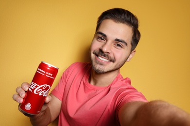 MYKOLAIV, UKRAINE - NOVEMBER 28, 2018: Young man taking selfie with Coca-Cola can on color background