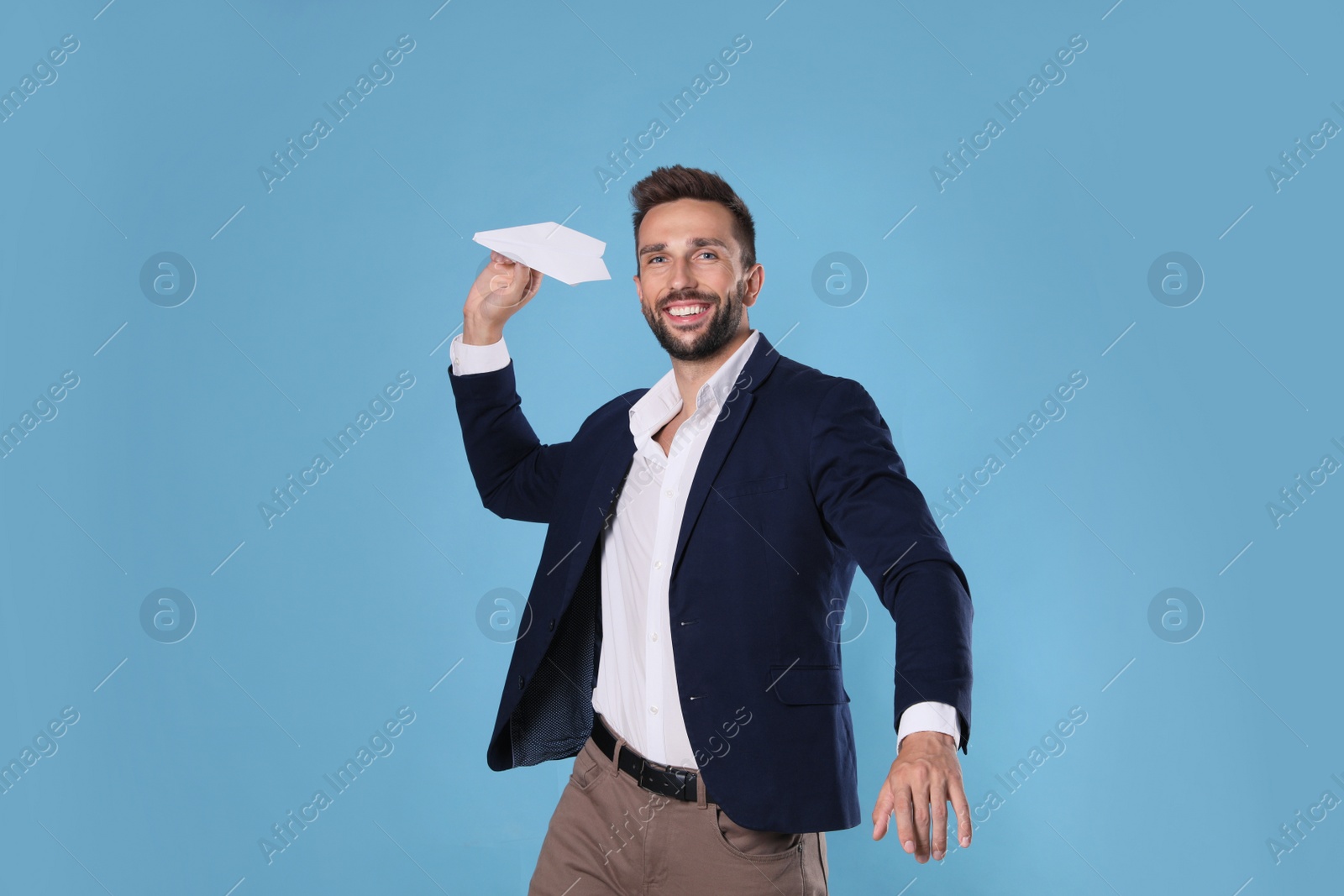 Photo of Handsome businessman playing with paper plane on light blue background