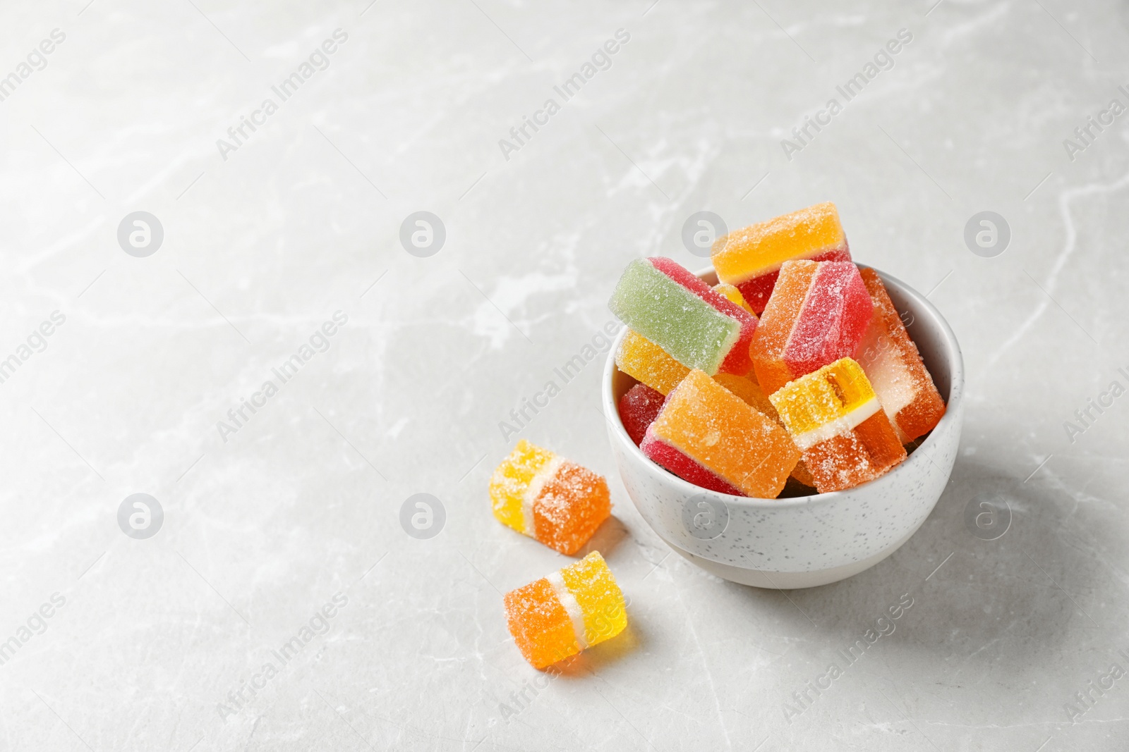 Photo of Bowl of delicious colorful candies on gray table with space for text