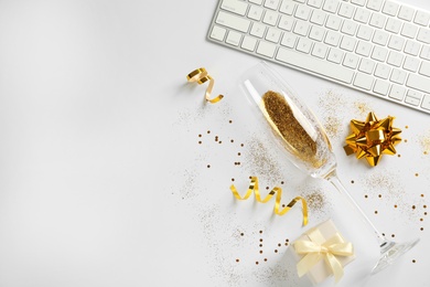 Photo of Composition of champagne glass with gold glitter, keyboard and gift box on white background, top view. Hilarious celebration