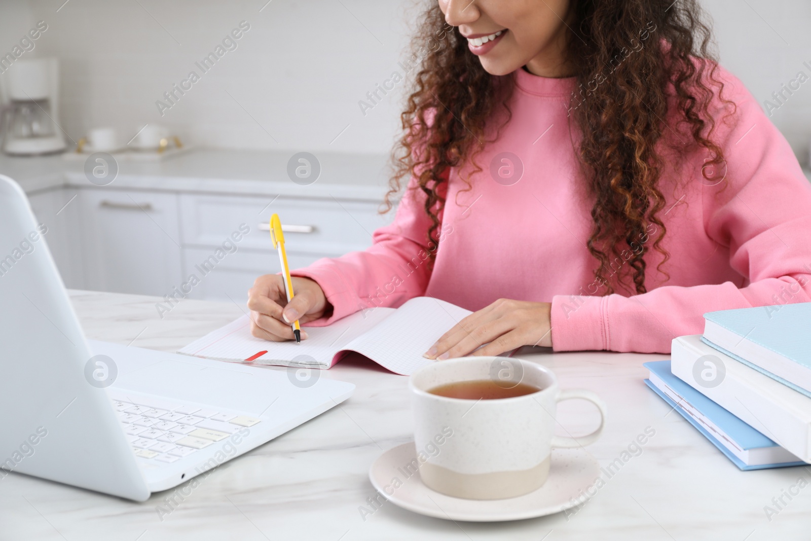 Photo of African American woman with modern laptop studying in kitchen, closeup. Distance learning