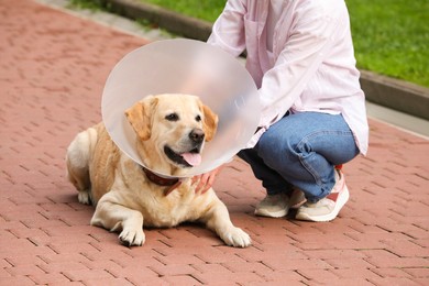 Photo of Woman with her adorable Labrador Retriever dog in Elizabethan collar outdoors, closeup