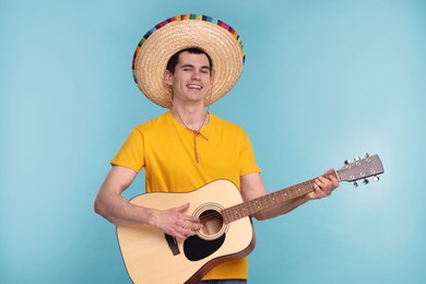 Photo of Young man in Mexican sombrero hat playing guitar on light blue background