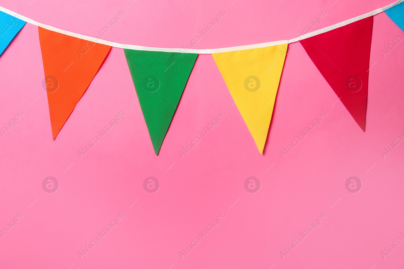 Photo of Bunting with colorful triangular flags on pink background. Space for text