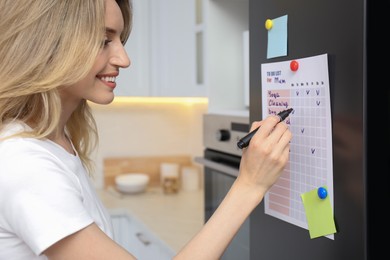 Photo of Young woman checking to do list on refrigerator door in kitchen