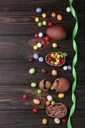 Tasty chocolate eggs and sweets on wooden table, flat lay