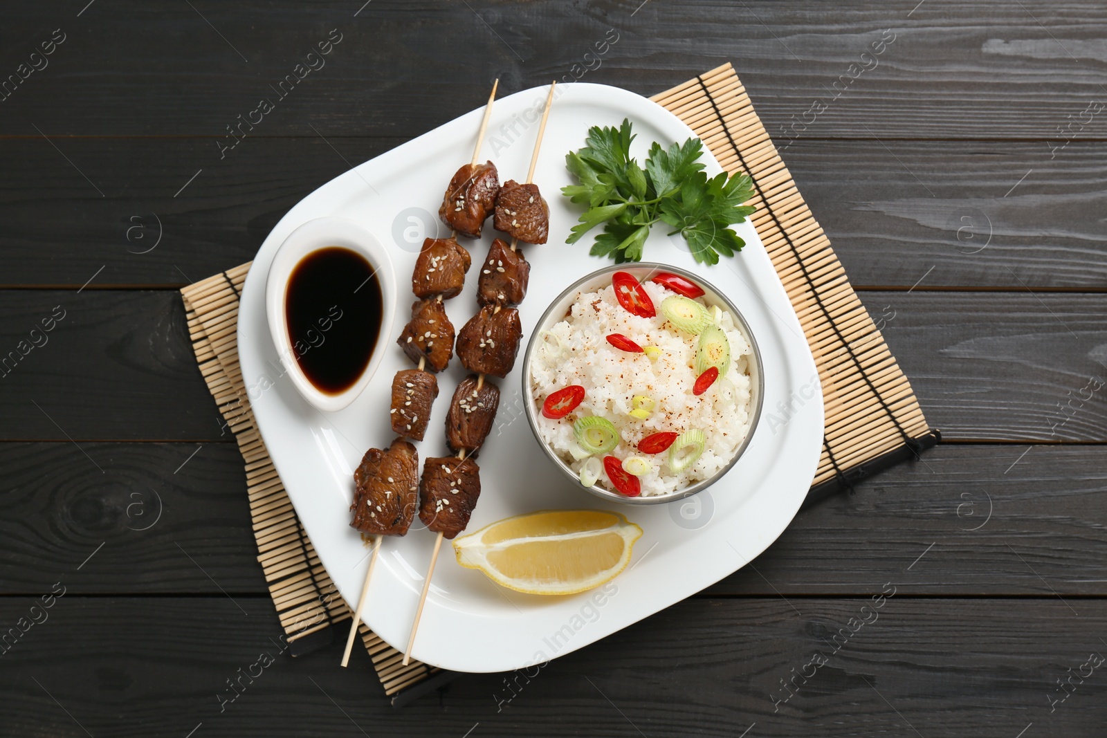Photo of Tasty chicken meat glazed in soy sauce served with rice on black wooden table, top view