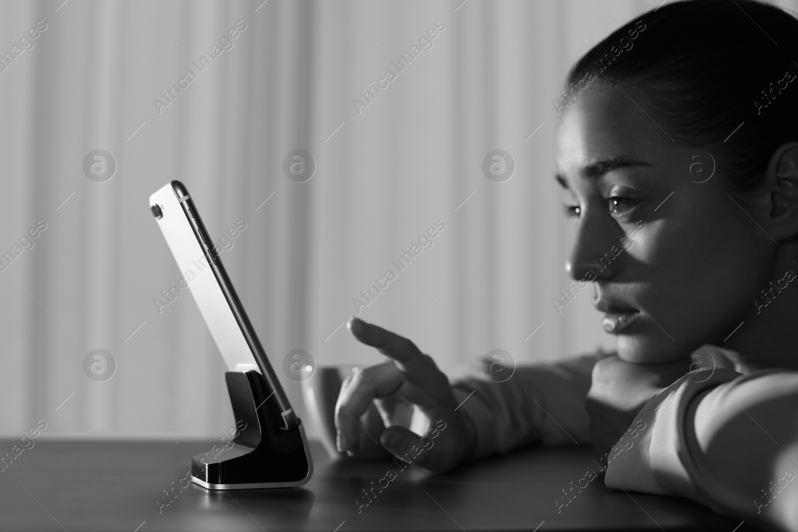 Photo of Upset woman with mobile phone at table indoors, black and white effect. Loneliness concept