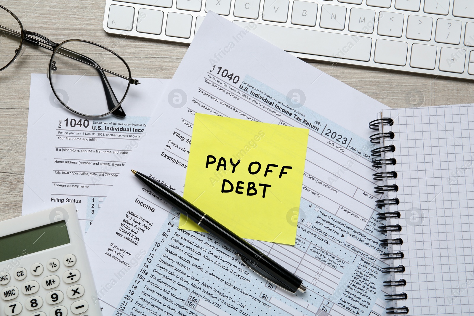 Image of Reminder note with phrase Pay Off Debt, documents, computer keyboard, glasses and calculator on wooden table, flat lay