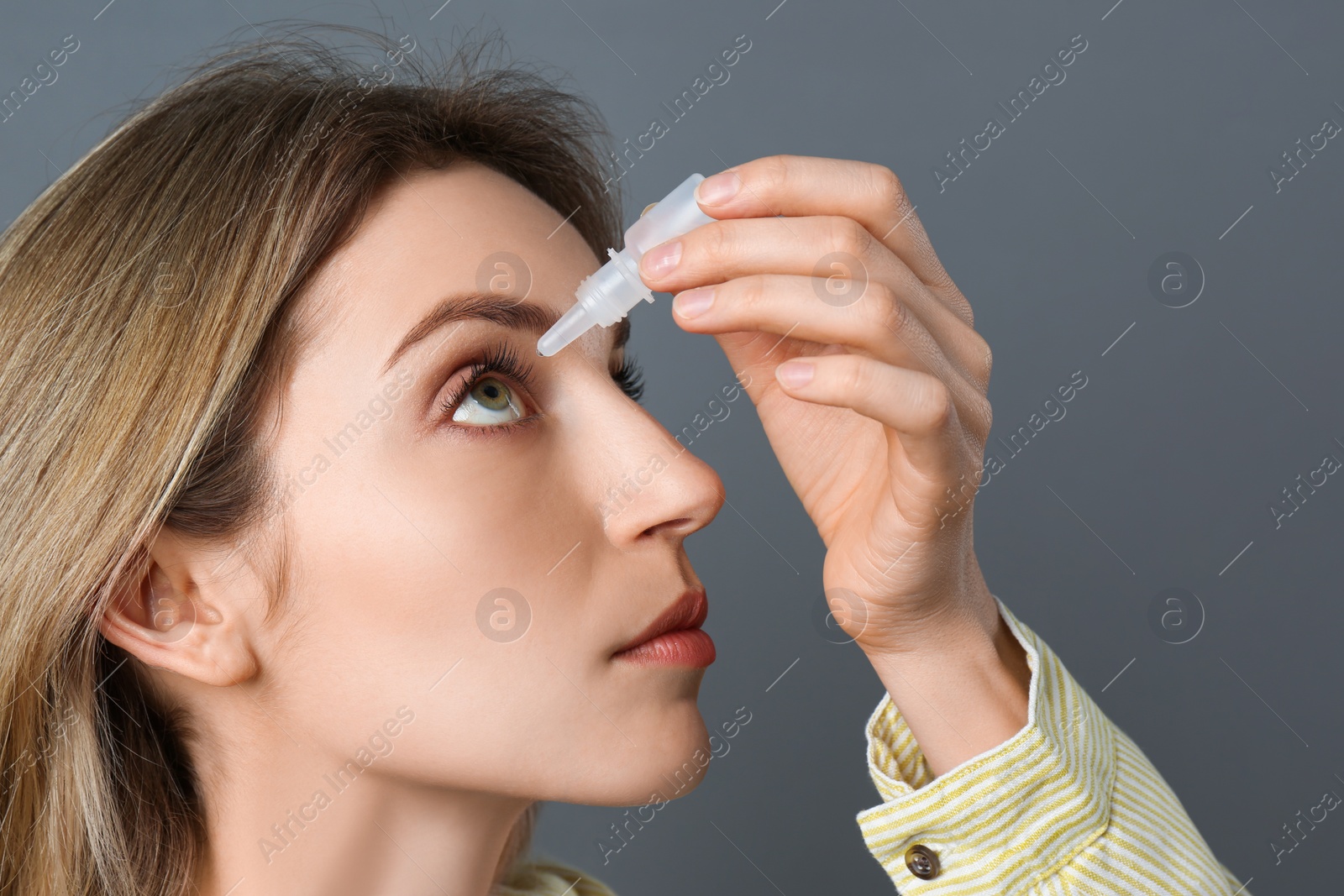 Photo of Young woman using eye drops on dark grey background, closeup