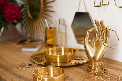 Photo of Composition with gold accessories and jewelry on dressing table near white wall