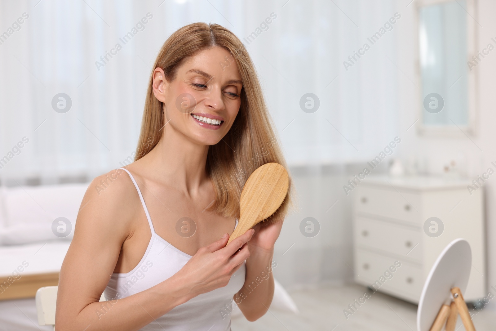 Photo of Beautiful woman brushing her hair near mirror in bedroom. Space for text