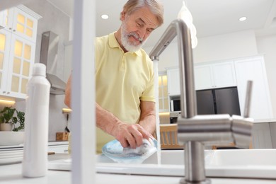 Photo of Senior man washing plate above sink in kitchen, view from outside