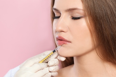 Photo of Young woman getting lips injection on color background, space for text. Cosmetic surgery