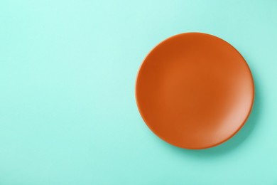 Photo of Clean orange plate on turquoise background, top view. Space for text